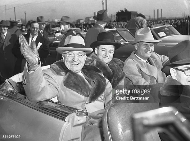 Left to right: President Harry S. Truman, wearing the new coat presented to him for the open car, 21 mile parade route to St. Paul, waves to the...
