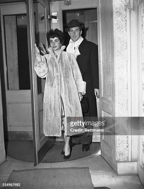 Michael Wilding and actress/wife, Elizabeth Taylor, are shown walking out of a buildings, in a revolving door.