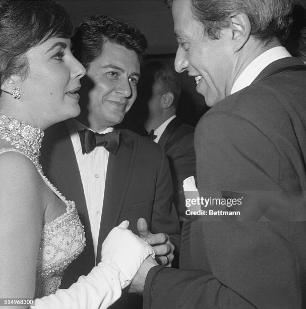 Tossing a party in New York, Elizabeth Taylor and husband Eddie Fisher greet one of their guests, comedian singer, and composer Adolph Green. The...