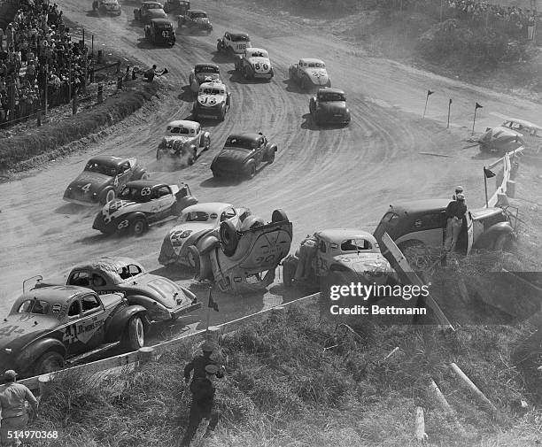 The remaining cars in a 100-mile modified and sports type stock car race at Daytona's speedway roar past the six entries involved in a chain reaction...