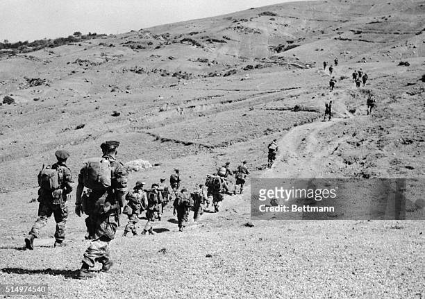 Equipment-laden paratroopers of the 5th French Foreign Legion Regiment strike out in Indian file across a rocky road here, in an effort to capture...