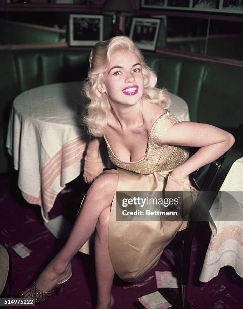 Jayne Mansfield in golden dress sits at a table.