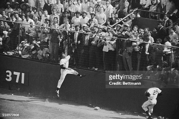 Giant centerfielder Willie Mays scales the right centerfield wall in an attempt to snare drive by Philadelphia's Harry Anderson in the ninth inning...