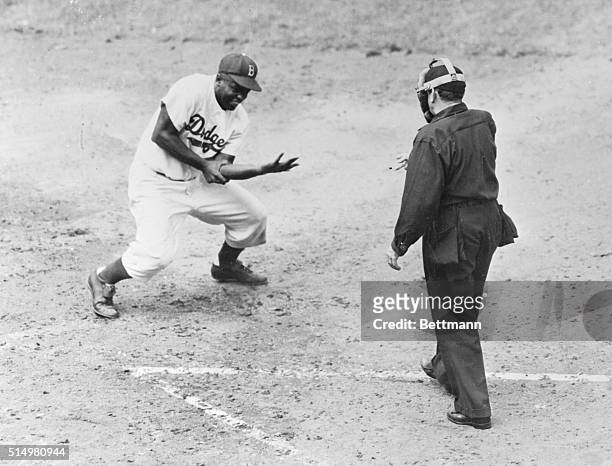 With umpire Ballanfant looking on, Jackie Robinson of the Brooklyn Dodgers is shown crouching down from the intense pain in his arm after he was hit...