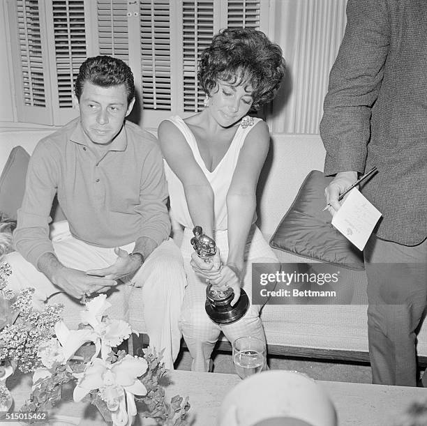 Beverly Hills, California: Actress Elizabeth Taylor apparently enthralled with her new won Oscar is shown with husband Eddie Fisher at a press...