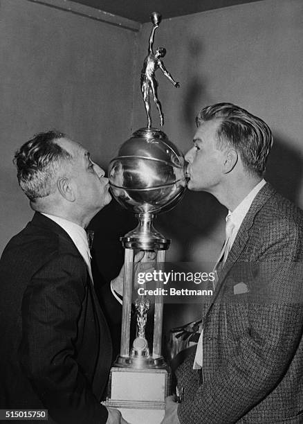 Owner Eddie Gottlieb of the Philadelphia Warriors, and coach George Sensky plant kisses on the trophy their team received after defeating Fort Wayne...