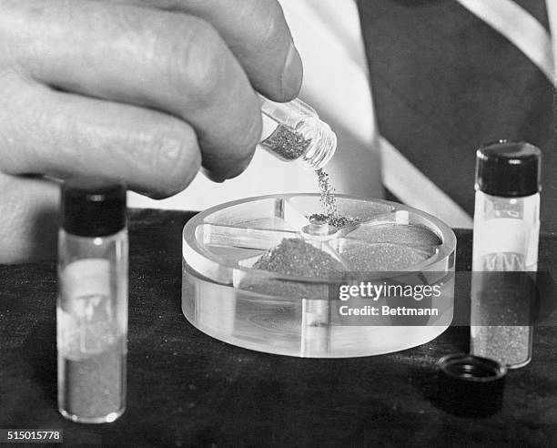 The hand of a General Electric scientist is pouring manmade diamonds into a container for presentation to the Smithsonian Institution. The plaque...