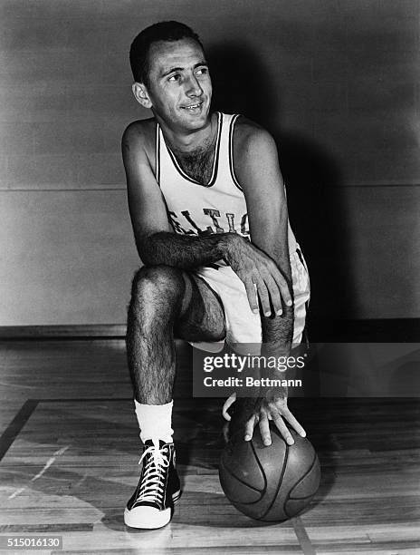 Bob Cousy, basketball player with the Boston Celtics, is shown posed, kneeling with the ball on the floor.