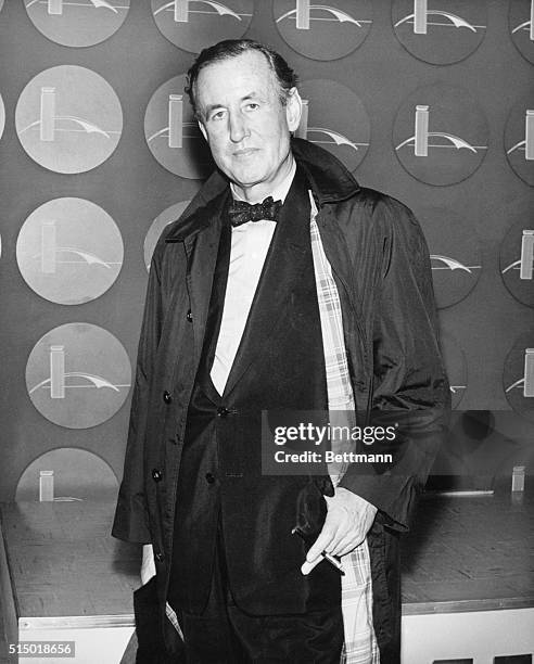 Picture shows the author of the James Bond series, Ian Fleming, posing in a tuxedo and over coat and smoking a cigarette.