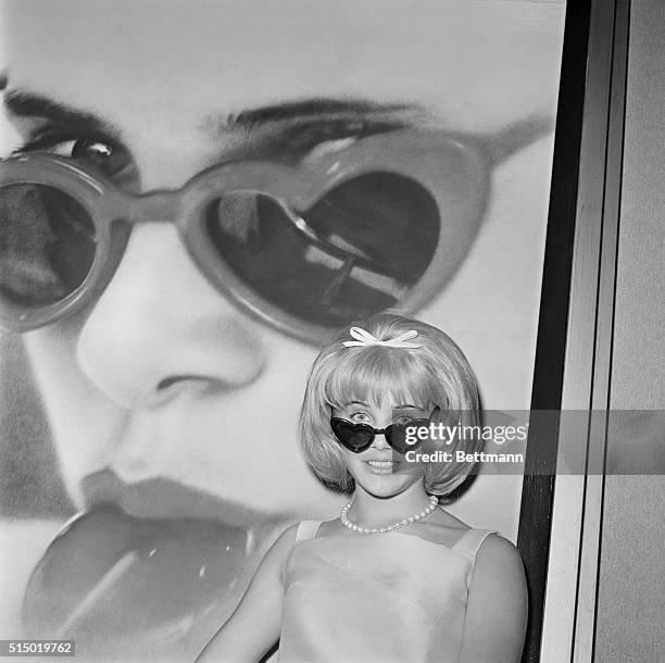 Sue Lyon who plays the title role in the film, Lolita is dwarfed by a huge photo mural of herself at invitational preview of the picture 6/21. Miss...