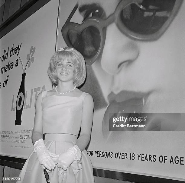 Sue Lyon who plays the title role in the film, Lolita is dwarfed by a huge photo mural of herself at invitational preview of the picture 6/21. Miss...