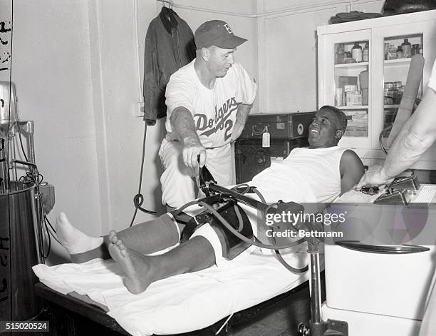 Manager Walter Alston of the Brooklyn Dodgers supervises the operation, as Jackie Robinson undergoes treatment for his ailing knee. The doohickey...