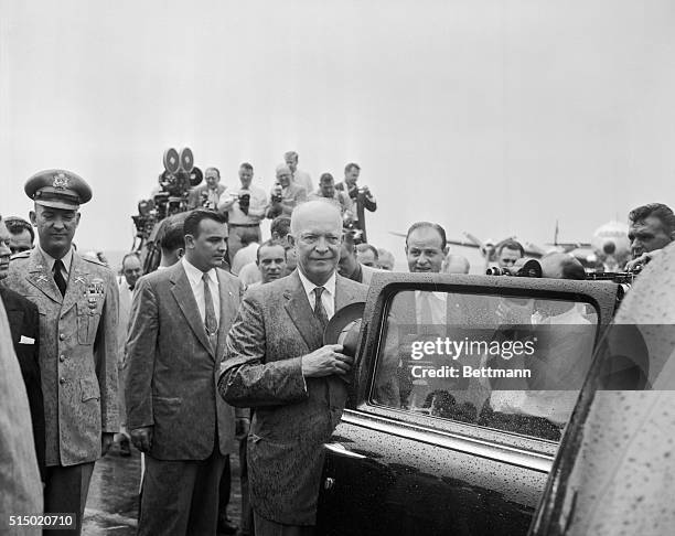 Home from the "Summit." Washington, D.C.: President Eisenhower stands with his hat over his heart in the driving rain as the band plays the national...