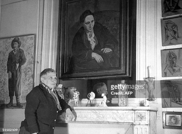 Writer Gertrude Stein poses in front of the portrait of her , at her Parisian apartment in an undated photograph.