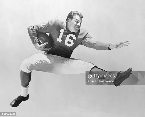 Frank Gifford of the New York Giants football team leaping, and holding football under right arm. .