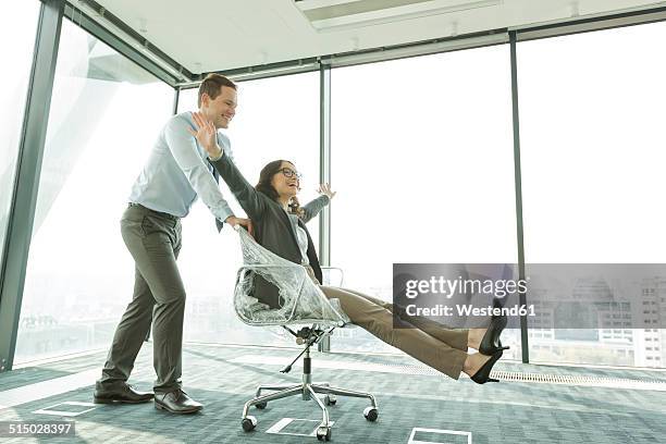 businessman pushing businesswoman in office chair - new from rolls press stock-fotos und bilder