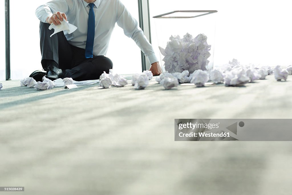 Businessman sitting on office floor surrounded by crumpled paper