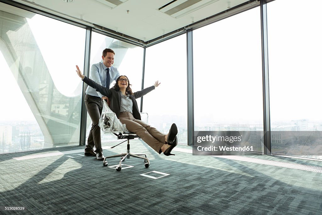 Businessman pushing businesswoman in office chair