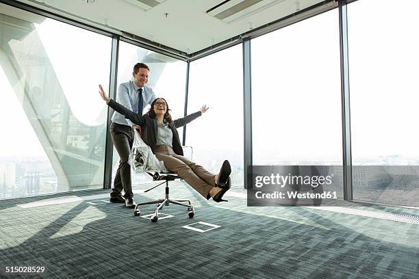 businessman pushing businesswoman in office chair - female founder stock pictures, royalty-free photos & images