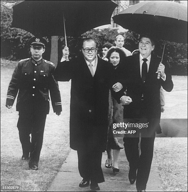 President Ronald Reagan and Chinese Premier Zhao Ziyang, both holding umbrellas, walk arm in arm, as Reagan escorts him to his car through the rain...