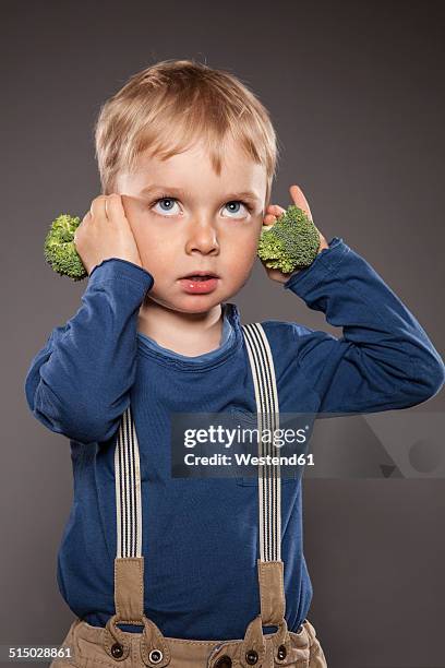 portrait of little boy holding broccoli on his ears - covering ears stock-fotos und bilder