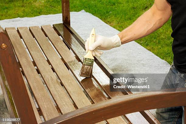 man applying glaze on wooden bench, partial view - garden furniture foto e immagini stock