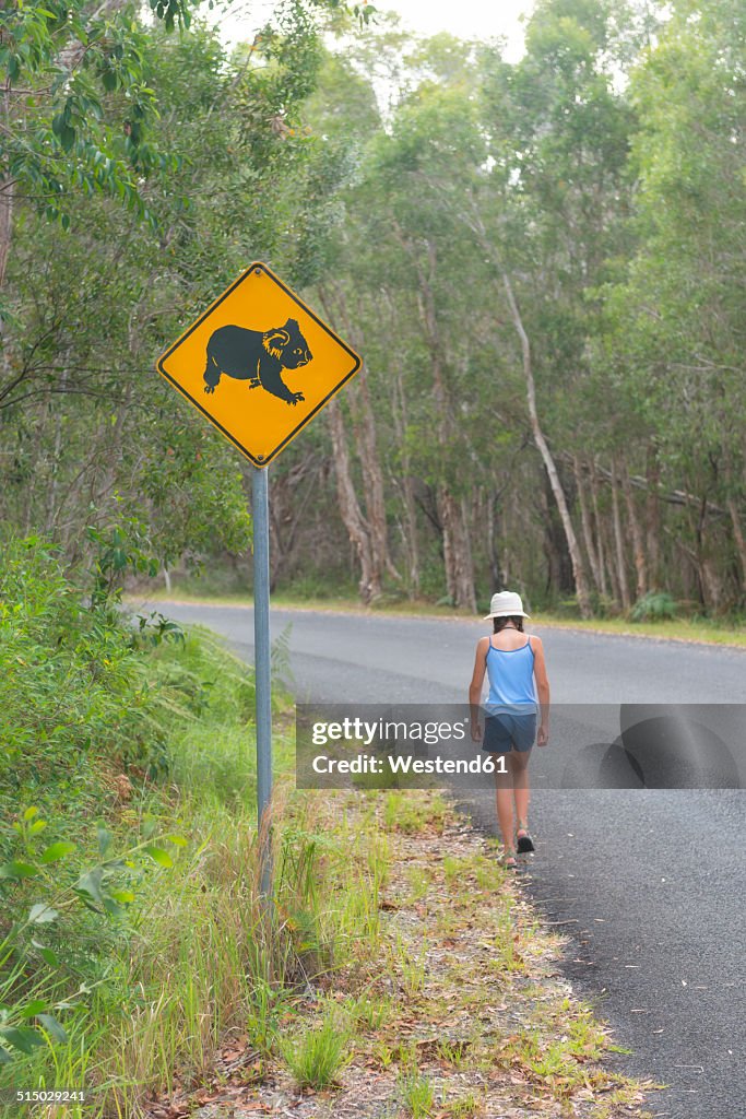Australia, New South Wales, Pottsville, roadsign with a koala bear and girl walking along road in Pottsville Environmental Park