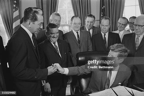 President John F. Kennedy passes the pen to Philippines Senator Rogelio de la Rosa during their signing into law of the $73 million Philippines War...