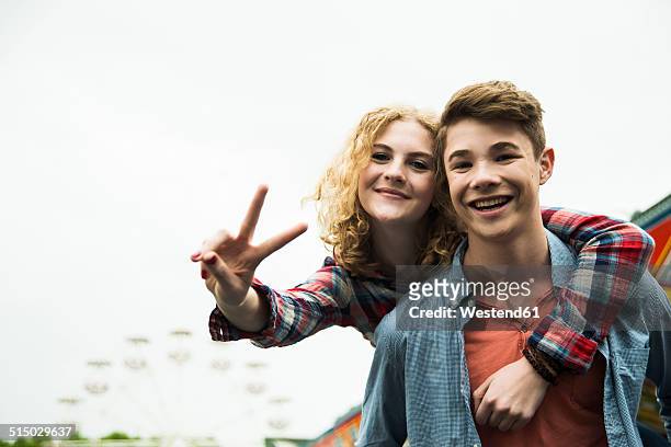 portrait of happy teenage couple showing victory-sign - arms around stockfoto's en -beelden