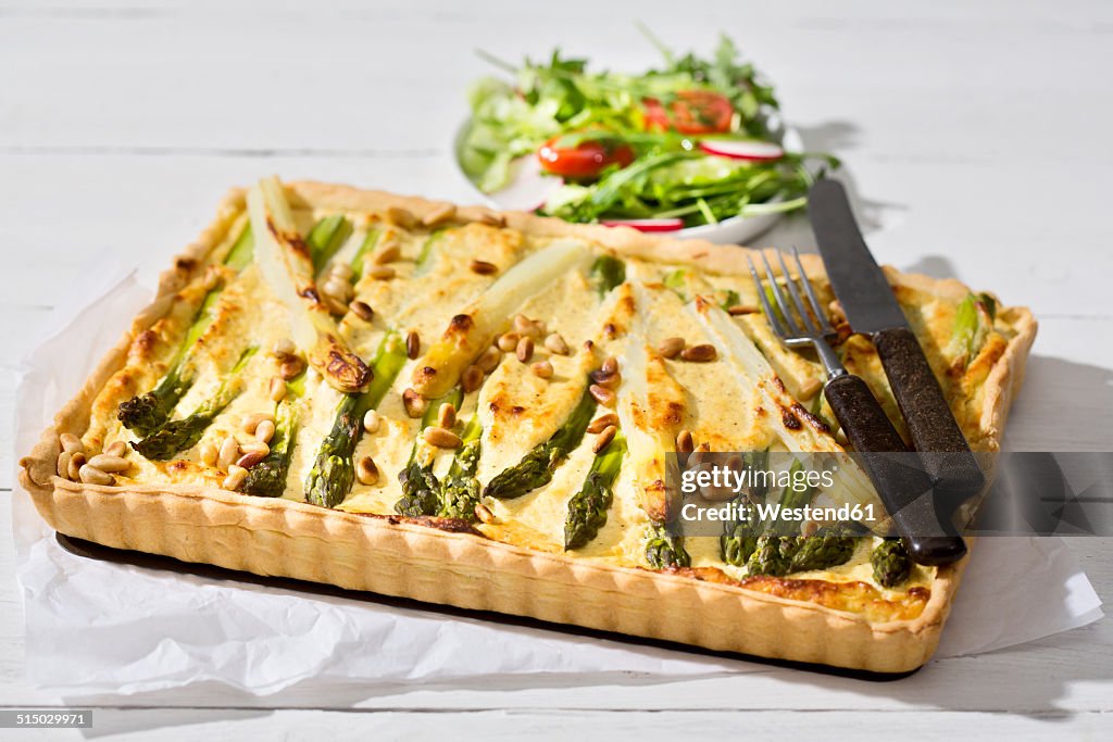 Asparagus tart, cutlery and lettuce dish on white wood