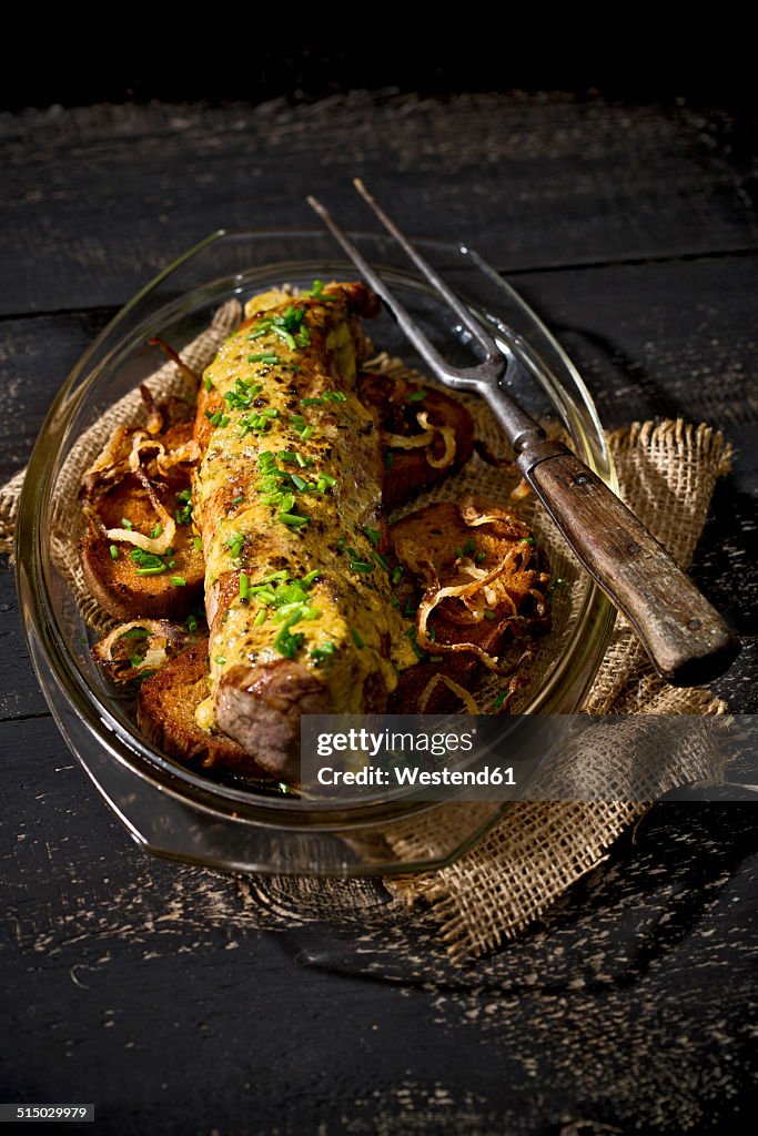 Fillet of pork on crusty bread with mustard herb butter and rucola, in a casserole dish