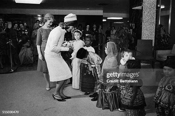 Mrs. Jacqueline Kennedy receives a bouquet and a polite bow from Richard Ong, of Malaya, as other children in Native costume look on, at the State...