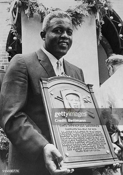 Smiling Jackie Robinson, who broke baseball's color line in 1947, holds a plaque after he was inducted into baseball's Hall of Fame here 7/23.