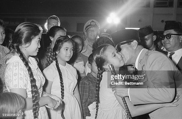 Surrounded by citizens of Jakarta, President Sukarno kisses his youngest daughter, Sukmawati, goodbye while his other daughters, Rachmawati and...