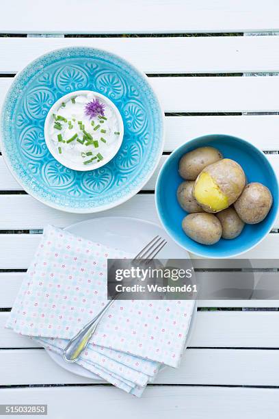 bowl of jacket potatoes and bowl of curd with herbs, cloth and fork on white wooden table - quark stock-fotos und bilder