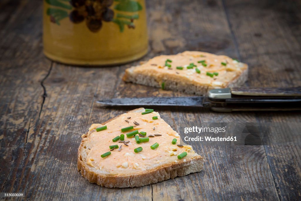 Two halves of slice of bread with obazda sprinkled with chives and knife on dark wood