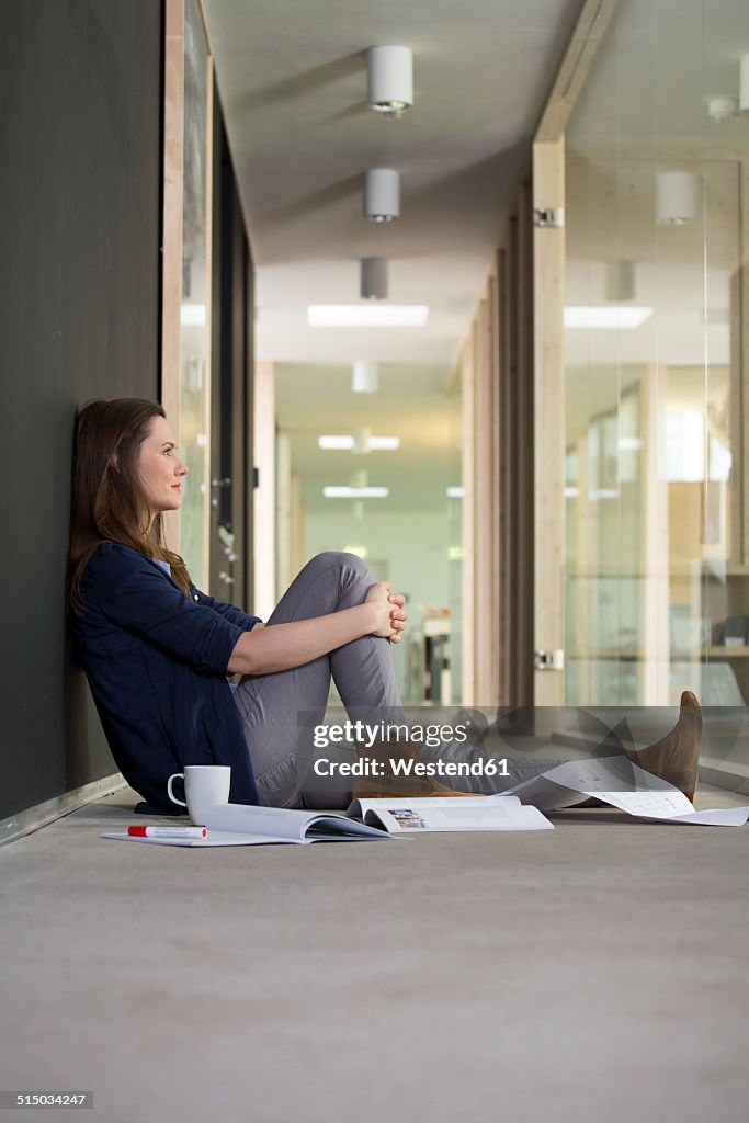 Portrait of business woman sitting on ground in corridor of office