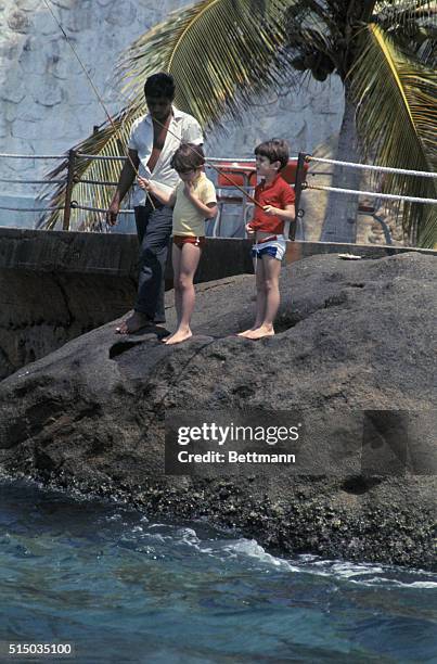 Servant baits hook as John F. Kennedy Jr. And his cousin, Anthony Radziwill, fish in the Pacific Ocean here March 19. Jacqueline Kennedy and her...