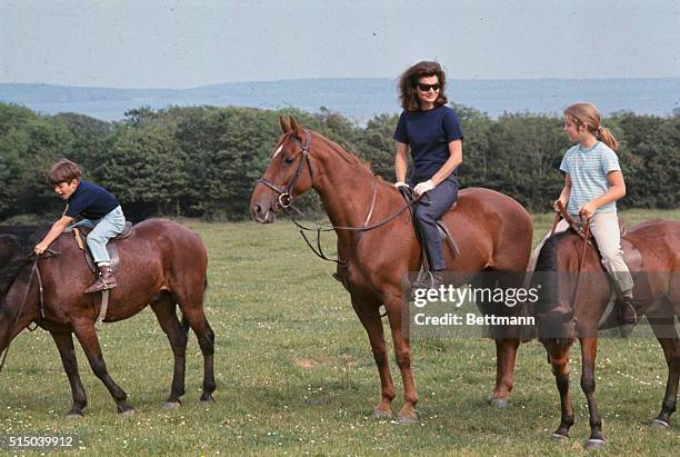 Mrs. John F. Kennedy, accompanied by her children, Caroline and John Jr., appear at press conference here June 16th on horseback. They are in Ireland...