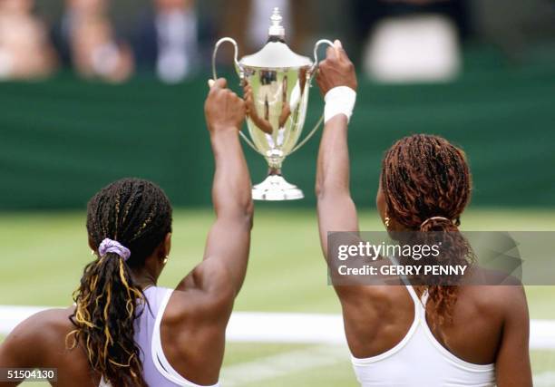 Sisters Venus and Serena Williams hold the Ladies' Doubles trophy after winning their final match at the Wimbledon 2000 tennis tournament against...