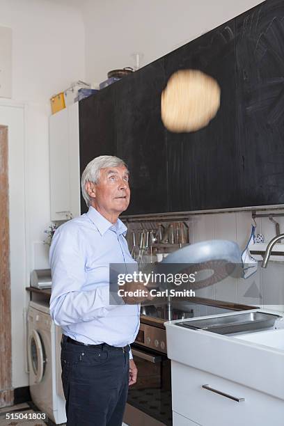 senior man tossing pancake on frying pan in kitchen at home - pancake toss stock-fotos und bilder