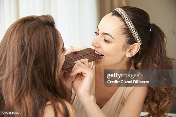 happy mother and daughter sharing large chocolate bar at home - sharing chocolate stock-fotos und bilder