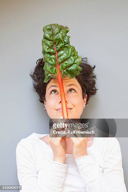 a woman holding rhubarb while looking at it over grey background - funny vegetable stockfoto's en -beelden