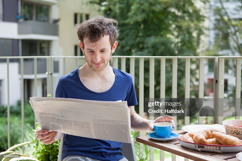 Young man reading newspaper while having breakfast at porch