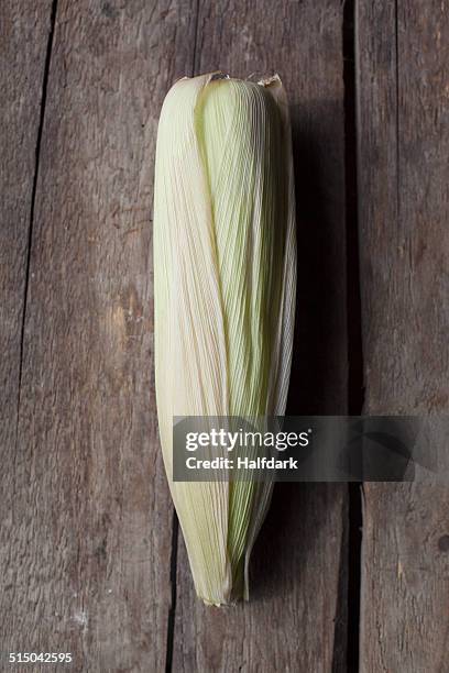 close-up of corn on the cob on wooden table - husk stock-fotos und bilder