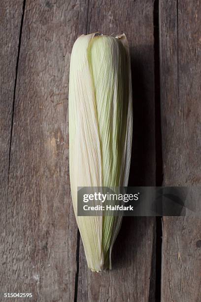 close-up of corn on the cob on wooden table - husk stockfoto's en -beelden