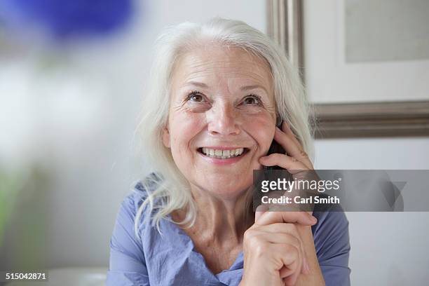 happy senior woman looking up while answering mobile phone at home - nur seniorinnen stock-fotos und bilder
