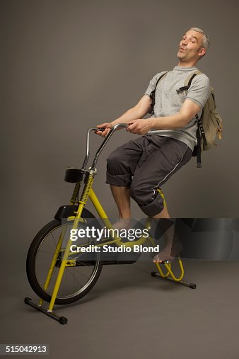 Full length of playful man on exercise bike against gray background Full length of playful man on exercise bike against gray background