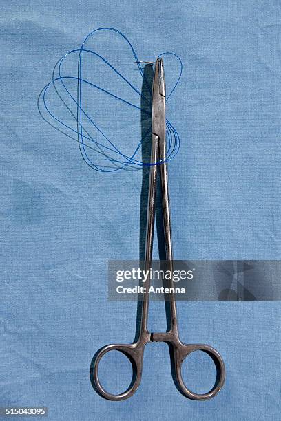 a pair of surgical scissors holding a suture needle and thread, directly above - surgical suture stock pictures, royalty-free photos & images