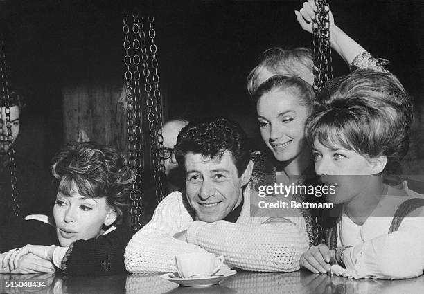 Innsbruck, Austria: Living It Up. U. S. Singer Eddie Fisher, surrounded by bevy of pretty actresses, rests his chin on his arms while sitting at bar...